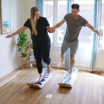Two people using SlackBoard balance boards in a home setting