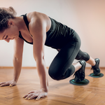 Woman performing mountain climber exercise with gliding discs on hardwood floor for core and cardio training